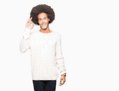 Afro saç giyen kış kazak el ve parmaklar ok işaretiyle yapıyor olumlu gülümseyen genç Afro-Amerikan adam. Başarılı ifade.