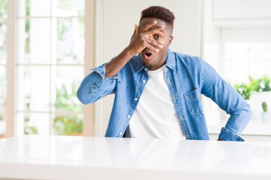 Yakışıklı afro-amerikan adam evde şok yüz ve gözleri el ile kapsayan gözetleme, utanmış ifade ile parmaklarından bakarak.