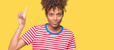 Güzel, genç, Afro-Amerikalı bir kadın izole edilmiş arka planda bir numarayı gösterip işaret ederken kendine güvenen ve mutlu bir şekilde gülümsüyor..