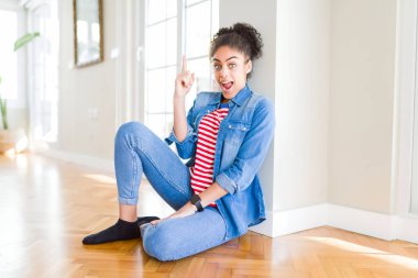 Afro saçlı güzel genç Afrikalı Amerikalı kadın yerde oturan başarılı bir fikir ile parmak yukarı işaret. Çıkıldı ve mutlu. Bir numara.