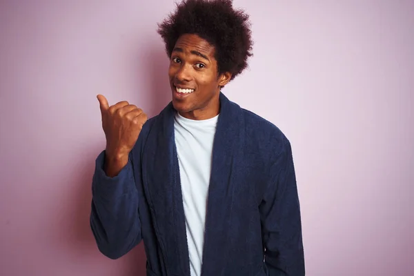 孤立したピンクの背景の上に立つパジャマを着た若いアフリカ系アメリカ人男性は 幸せそうな顔で微笑み 親指を上げて横を向いている — ストック写真