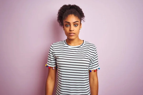 African american woman wearing navy striped t-shirt standing over isolated pink background with serious expression on face. Simple and natural looking at the camera.