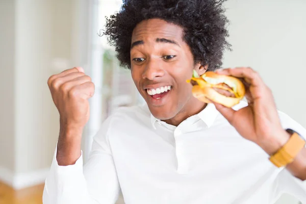 アフリカ系アメリカ人の空腹の男は 昼食のためにハンバーガーを食べて誇らしげに叫び 勝利と成功を祝う非常に興奮し 感情を応援 — ストック写真