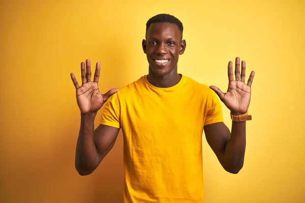 カジュアルなTシャツを着た若いアフリカ系アメリカ人男性は 自信を持って幸せに微笑みながら 10番の指を見せ 指で指を上げている黄色の背景の上に立っている — ストック写真