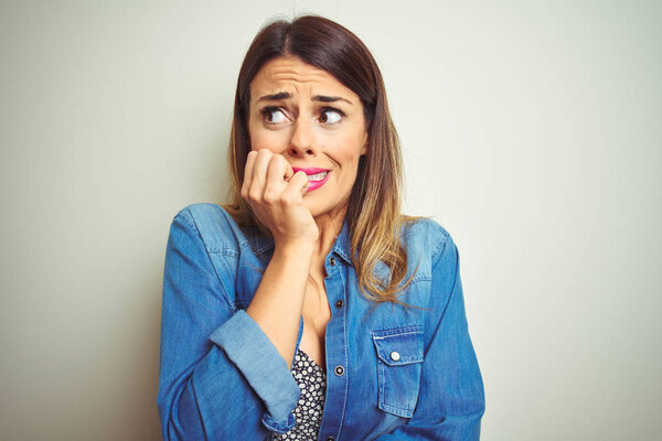 Молодая красивая женщина, стоящая на изолированном фоне, выглядящая напряженной и нервной с руками на губах, грызущими ногти. Проблема тревоги
.