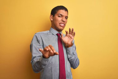 Genç yakışıklı Arap işadamı gömlek giyen ve izole sarı arka plan üzerinde kravat tiksinti ifade, hoşnutsuz ve korkulu tiksinti yüz yapıyor çünkü nefret tepki. Elleri havada. Sinir bozucu kavram.