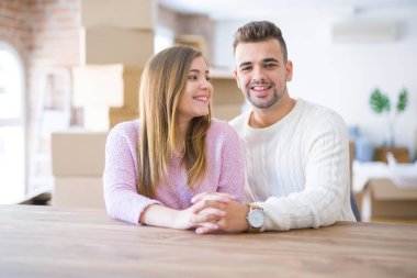 Evde masada oturan genç güzel çift, onların arkasında karton kutular ile yeni eve hareket için çok mutlu aşık sarılmak