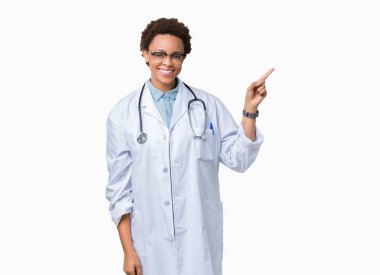 Yüz üzerinde büyük bir gülümseme ile izole arka plan üzerinde tıbbi ceket giyen genç Afrikalı Amerikan doktor kadın, kamera bakarak yan el ve parmak ile işaret.