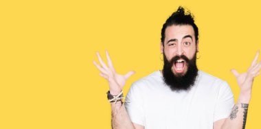 Uzun saçlı ve sakal ile genç hipster adam rahat beyaz t-shirt çılgın kutluyor ve başarı için hayran silah kaldırdı ve açık gözleri heyecanlı çığlık giyiyor. Kazanan kavramı