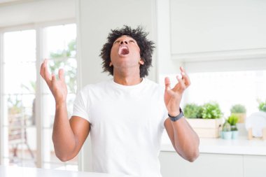 Genç Afrikalı Amerikalı adam rahat beyaz t-shirt evde oturan deli ve deli çığlık ve agresif ifade ve kollar ile bağırarak kaldırdı giyiyor. Hayal kırıklığı kavramı.