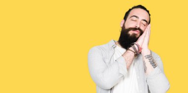 Uzun saç, sakal ve uyku yorgun hayal ve ile gülümseyen gözleri kapalı iken ellerle birlikte poz küpe ile genç adam.