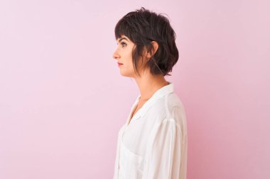 Yan bakan izole pembe arka plan üzerinde duran beyaz gömlek giyen genç güzel kadın, kendine güvenen gülümseme ile doğal yüzü ile profil poz dinlenmek.
