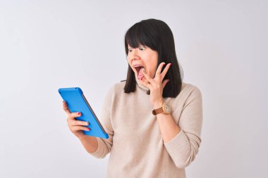 Izole beyaz arka plan üzerinde duran mavi tablet kullanan güzel Çinli kadın çok mutlu ve heyecanlı, kazanan ifade büyük bir gülümseme ile çığlık zafer kutluyor ve ellerini kaldırdı