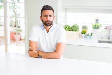 Yakışıklı İspanyol ev şüpheci ve sinir, onaylamayan ifade yüz çapraz kolları üzerinde rahat beyaz t-shirt dostum. Negatif kişi.