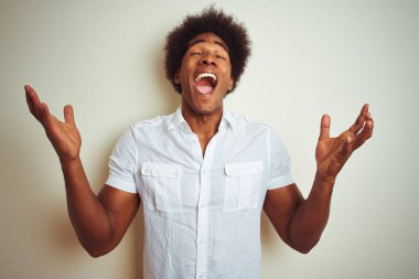 Afro saç ile Afrikalı Amerikan adam izole beyaz arka plan üzerinde dikilmiş gömlek ayakta deli ve silah ile başarı için deli kutluyor kaldırdı ve heyecanlı çığlık kapalı gözleri. Kazanan kavramı
