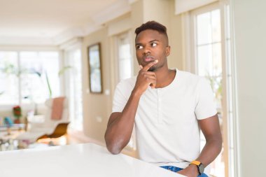 Çene düşünme hakkında soru, dalgın ifade üzerine el ile yakışıklı Afrikalı-Amerikalı adam evde beyaz masada. Düşünceli yüzüyle gülümsüyor. Şüphe kavramı.