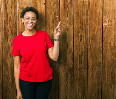 Kameraya bakarak yan el ve parmak ile işaret yüzünde kocaman bir gülümseme ile izole arka plan üzerinde gözlük güzel genç Afro-Amerikan kadın.