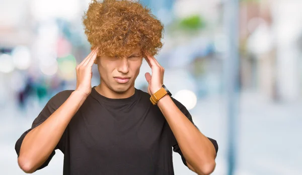 ストレスのため頭の痛みに頭を抱えた黒いTシャツを着たアフロヘアの若いハンサムな男 苦しむ片頭痛 — ストック写真