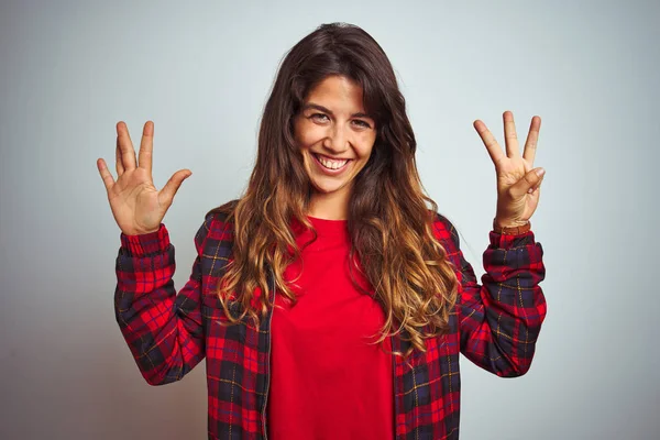 Beyaz izole arka plan üzerinde ayakta kırmızı t-shirt ve ceket giyen genç güzel kadın gösteren ve parmak numarası sekiz ile işaret kadar emin ve mutlu gülümseyen.