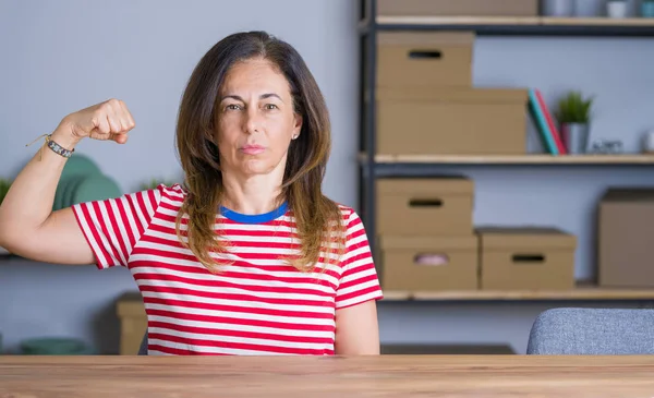 Orta yaş kıdemli kadın evde masada oturan güçlü kişi kol kas gösteren, emin ve güç gurur