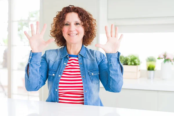 Kıvırcık saçlı orta yaş yaşlı kadın evde kot ceket giyen gösteren ve parmakları ile işaret ederken emin ve mutlu gülümseyerek on numara.