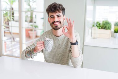 Genç adam sabah parmaklarıyla ok işareti yapıyor kahve bir fincan içme, mükemmel sembolü