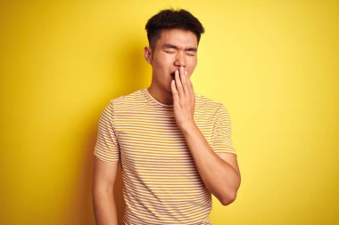 Genç Asya Chinese adam giyen t-shirt ayakta üzerinde izole sarı arka planda bored esneme yorgun kapsayan ağız ile el. Huzursuz ve uykululuk.