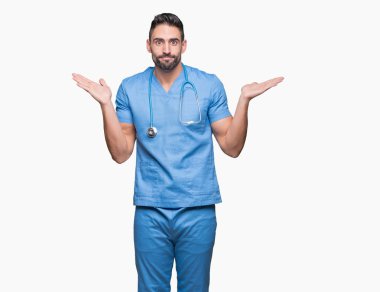 Yakışıklı genç doktor cerrah adam izole arka plan clueless ve şaşkın bir ifadeyle kollar ve eller kaldırdı. Şüphe kavramı.