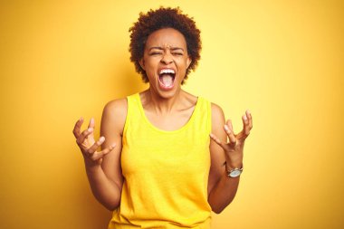 Beauitul Afrikalı Amerikan kadın izole sarı arka plan üzerinde yaz t-shirt giyiyor çılgın ve deli bağırma ve agresif ifade ve silah ile bağırdı kaldırdı. Hayal kırıklığı kavramı.