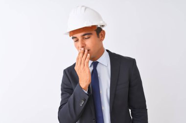Genç yakışıklı mimar adam izole beyaz arka plan üzerinde takım elbise ve kask giyen el ile ağız kapsayan yorgun esneme sıkılmış. Huzursuz ve uykululuk.