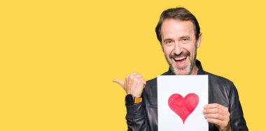 İşaret ve başparmak kadar mutlu yüz gülümseyen tarafı ile gösterilen Kırmızı kalp ile kağıt tutan yakışıklı orta yaş erkek