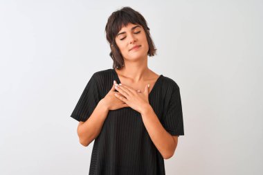 Siyah t-shirt giyen genç güzel kadın kapalı gözleri ve yüzünde minnettar jest göğüs elleri ile gülümseyerek izole beyaz arka plan üzerinde duran. Sağlık kavramı.