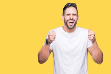 Genç adam izole arka plan üzerinde rahat beyaz t-shirt giyen silah ile başarı için heyecanlı kutlamak zafer gülümseyen kaldırdı. Kazanan kavramı.