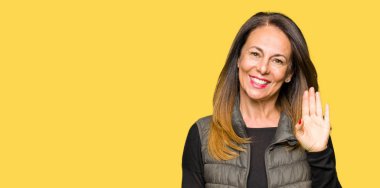 Orta yaş kadın giyiyor kış mutlu selam Waiving yelek ve gülümseyen, dostça jest hoş geldiniz güzel