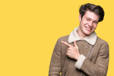Yakışıklı delikanlı izole arka neşeli bir gülümseme ile yüz el ve parmak kadar mutlu ve doğal ifade yüzünde yanında işaret içinde kış palto giyiyor