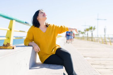 Güzel genç kadın deniz tarafından bir gezinti üzerinde oturan gülümseyen 