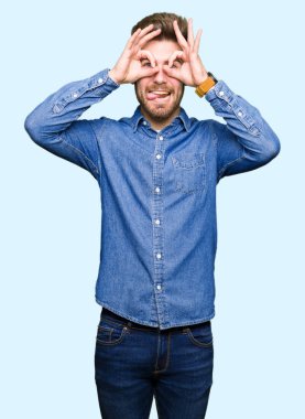Rahat denim gömlek giyen genç yakışıklı sarışın adam dürbün yapışması gibi ok jest yapıyor, gözleri parmaklarla bakıyor. Çılgın ifade.