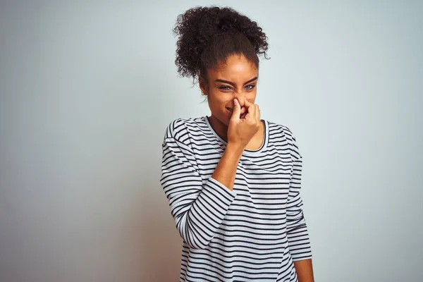 African american woman wearing navy striped t-shirt standing over isolated white background smelling something stinky and disgusting, intolerable smell, holding breath with fingers on nose. Bad smells concept.