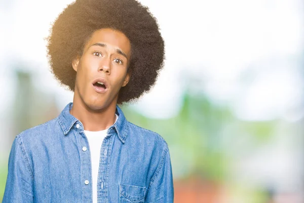 Young african american man with afro hair In shock face, looking skeptical and sarcastic, surprised with open mouth