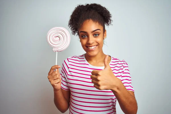 アフリカ系アメリカ人のティーンエイジャーの女性は 孤立した白い背景の上にカラフルなキャンディーを食べて Okサインをやって大きな笑顔で幸せ 指で親指アップ 優れた兆候 — ストック写真