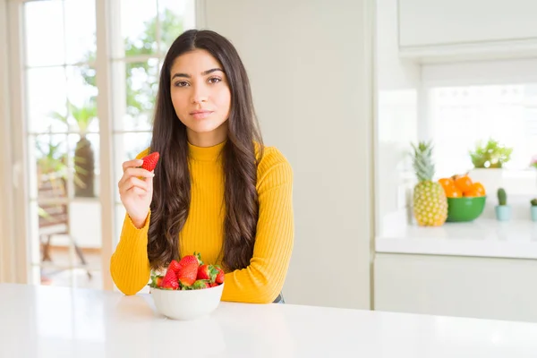 真剣に考えるスマートな顔に自信のある表情で健康的なスナックとして新鮮な赤いイチゴを食べる若い女性 — ストック写真