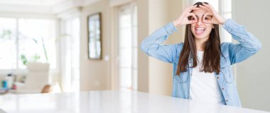 Güzel genç kadının evde beyaz masada oturan geniş açı resim dürbün yapışması gibi ok jest yapıyor, gözler parmaklarla bakıyor. Çılgın ifade.