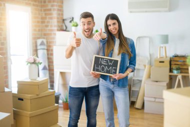 Genç güzel çift ok işareti yapıyor büyük bir gülümseme ile mutlu yeni evde yeni ev metin ile kara tahta tutan, parmaklarla başparmak, mükemmel işareti
