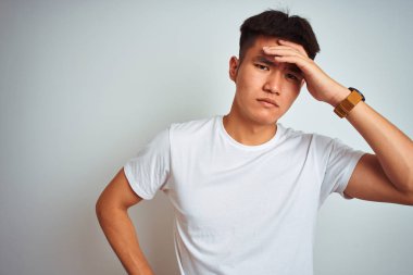 İzole beyaz arka plan üzerinde ayakta t-shirt giyen genç Asyalı Çinli adam endişeli ve alnında el, sinir ve kriz için endişeli bir sorun hakkında vurguladı