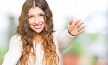 Sarılmak için Kollarını açarak gülümseyerek kameraya bakarak beyaz kazak giyen genç güzel kadın. Neşeli ifade kucaklayan mutluluk.