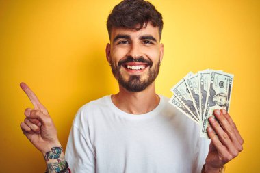 Dövme tutan genç adam izole sarı arka planda ayakta çok mutlu yan el ve parmak ile işaret