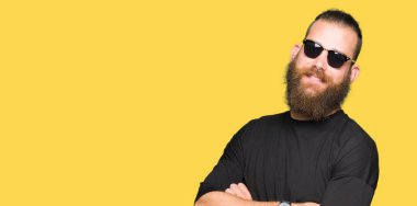 Kameraya bakarak çapraz silah ile gülümseyen güneş gözlüğü mutlu yüz giyen genç hipster adam. Olumlu bir kişi.