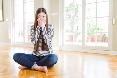 Evde çıplak yalınayak oturan güzel Asyalı kadın yanlışlık için eller ile ağız kapsayan şok. Gizli konsept.