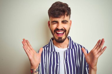 Dövme ile genç adam izole beyaz arka plan üzerinde ayakta çizgili gömlek dikilmiş silah ile başarı için deli ve çılgın kutluyor ve kapalı gözleri heyecanlı çığlık kaldırdı. Kazanan kavramı