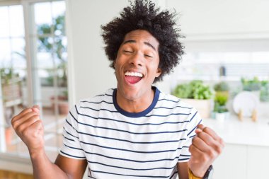 Çizgili t-shirt giyen Afrikalı Amerikalı adam çok mutlu ve heyecanlı silah ile kazanan jest yaparak, gülümseyen ve başarı için çığlık kaldırdı. Kutlama konsepti.